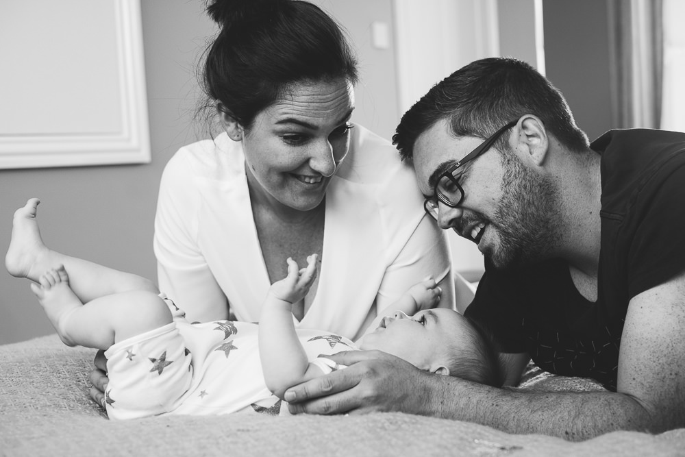 Godstone Surrey Family Photographer parents and baby on bed natural light lifestyle portrait laughing black and white
