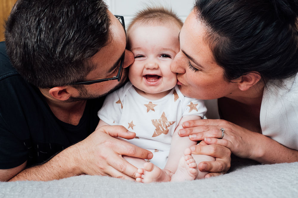 Godstone Surrey Family Photographer parents and baby kissing on cheek on bed natural light lifestyle portrait